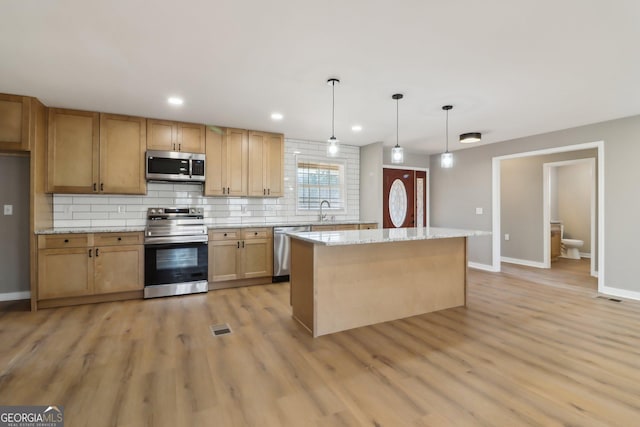 kitchen with light wood finished floors, a sink, stainless steel appliances, backsplash, and a center island