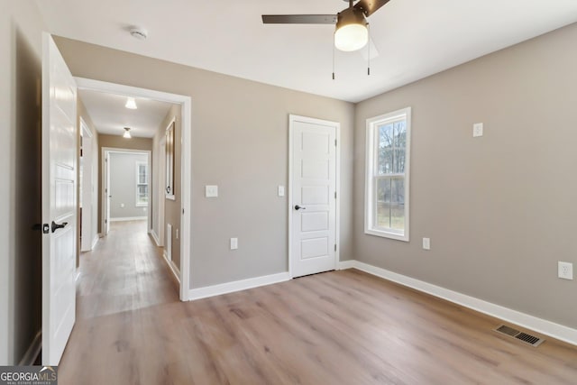 unfurnished bedroom with a ceiling fan, light wood-style flooring, visible vents, and baseboards