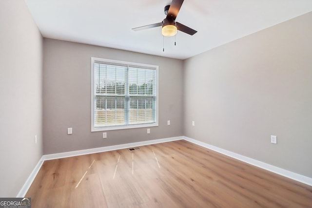 unfurnished room with wood finished floors, a ceiling fan, visible vents, and baseboards