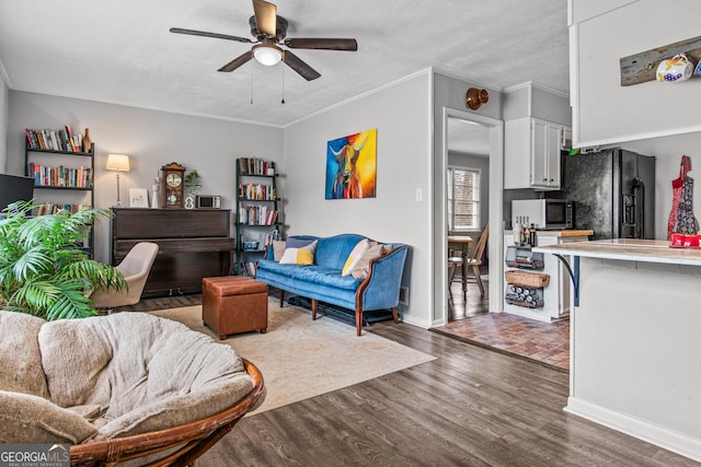 living area featuring dark wood-style floors, baseboards, a ceiling fan, and crown molding