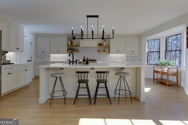 kitchen with a kitchen island with sink, light wood-style floors, white cabinets, open shelves, and tasteful backsplash