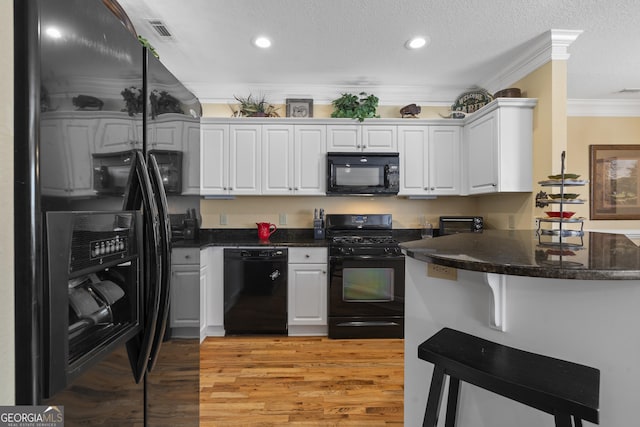 kitchen with crown molding, light wood finished floors, visible vents, white cabinetry, and black appliances