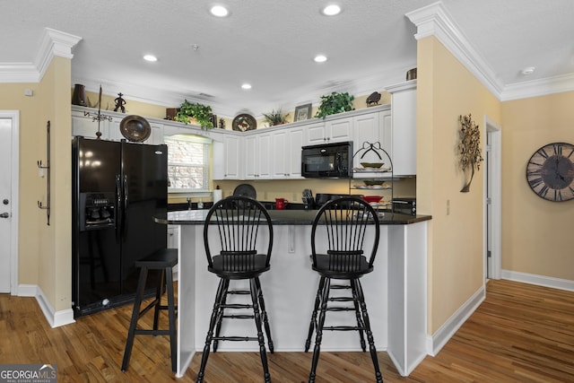 kitchen with dark countertops, white cabinetry, black appliances, a peninsula, and a kitchen breakfast bar