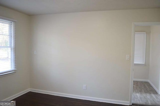 empty room with dark wood-style flooring, a healthy amount of sunlight, and baseboards