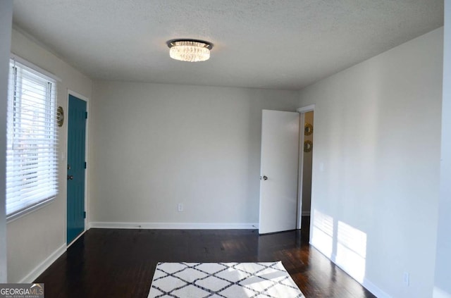 spare room featuring a textured ceiling, dark wood finished floors, and baseboards