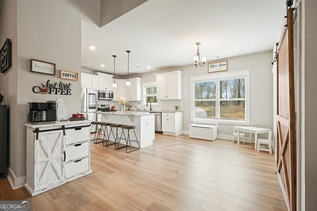 1312 Mcgarity Rd, Temple, GA 30179 - kitchen featuring a barn door, stainless steel appliances, a kitchen breakfast bar, white cabinetry, and tasteful backsplash