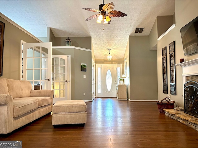 living area with a textured ceiling, a fireplace, visible vents, baseboards, and dark wood finished floors