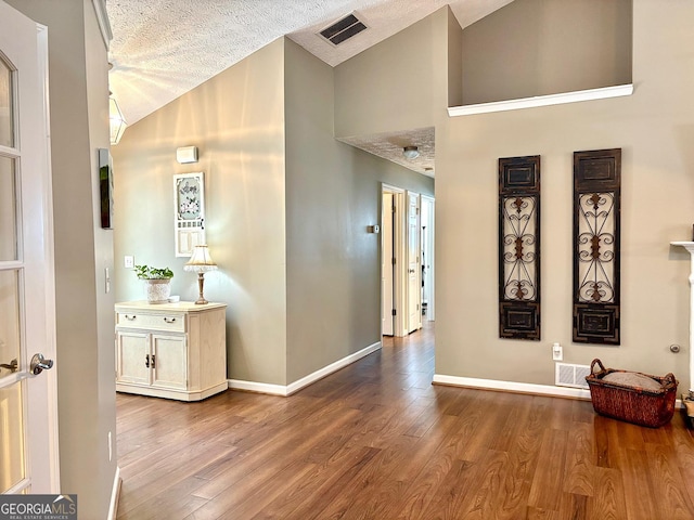 hallway with visible vents, a textured ceiling, baseboards, and wood finished floors