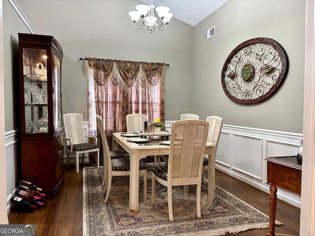 dining space featuring dark wood-style floors, a wainscoted wall, visible vents, and an inviting chandelier