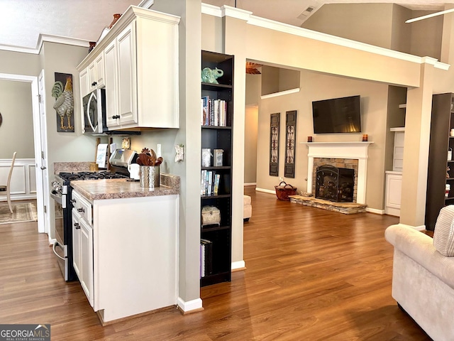 kitchen with stainless steel appliances, white cabinetry, a stone fireplace, and wood finished floors