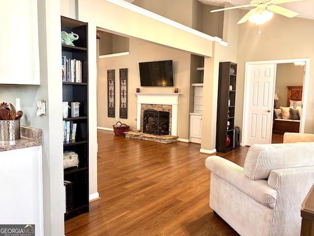 living area with baseboards, ceiling fan, wood finished floors, a stone fireplace, and built in shelves