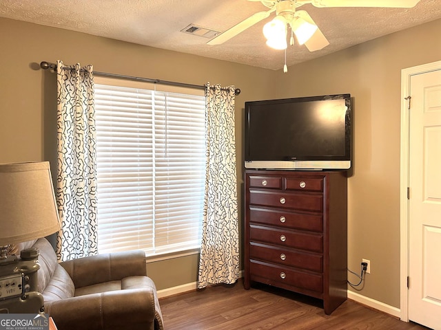 living area featuring a textured ceiling, wood finished floors, visible vents, baseboards, and a ceiling fan