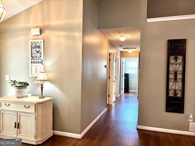 hallway featuring visible vents, dark wood finished floors, a textured ceiling, and baseboards