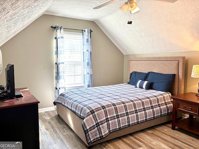 bedroom featuring light wood finished floors, lofted ceiling, ceiling fan, a textured ceiling, and baseboards