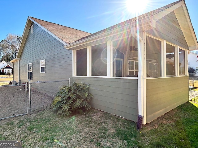 view of property exterior featuring a shingled roof, a sunroom, and fence