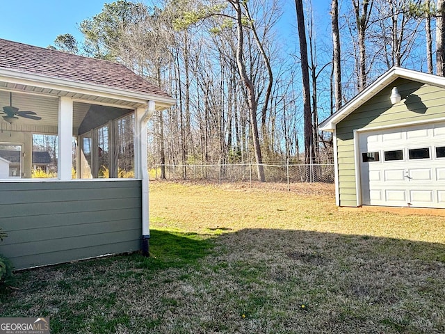 view of yard with a garage, an outdoor structure, fence, a sunroom, and a ceiling fan