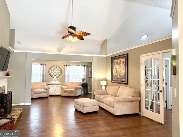 living area featuring dark wood-style floors, lofted ceiling, a fireplace with raised hearth, ornamental molding, and ceiling fan