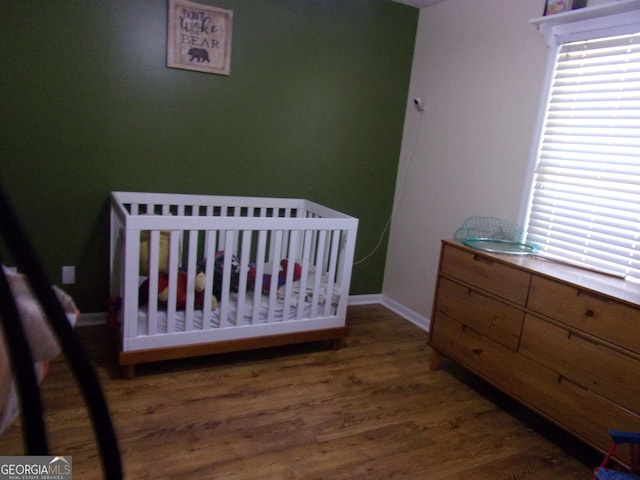 bedroom featuring a nursery area, multiple windows, baseboards, and wood finished floors