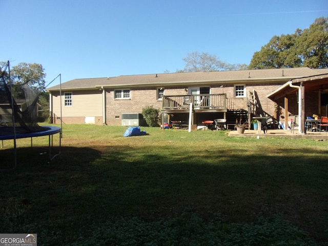 rear view of house featuring a deck, central air condition unit, brick siding, a lawn, and a trampoline