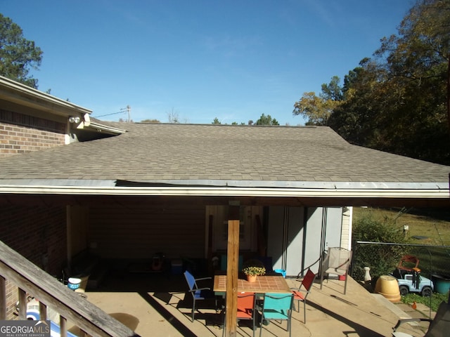 exterior space with a patio area, roof with shingles, and brick siding