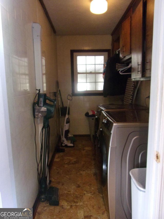 laundry area with cabinet space, separate washer and dryer, and tile walls