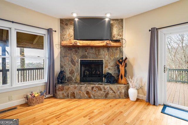 living room with a stone fireplace, wood finished floors, visible vents, and baseboards