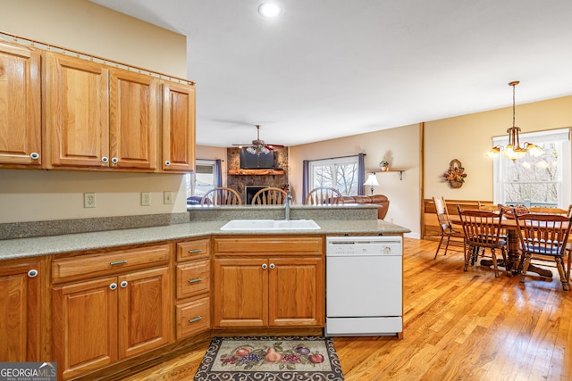 kitchen featuring a stone fireplace, light wood-style flooring, a peninsula, a sink, and dishwasher