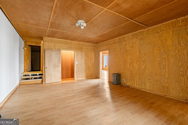 unfurnished living room featuring wood walls, baseboards, and wood finished floors