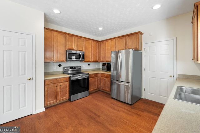 kitchen featuring appliances with stainless steel finishes, brown cabinetry, light countertops, and dark wood-style floors