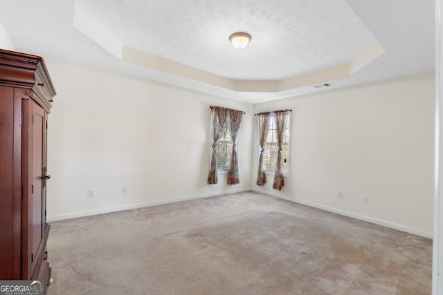 spare room with a raised ceiling, visible vents, light colored carpet, a textured ceiling, and baseboards