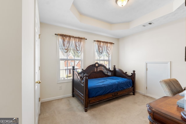 bedroom with light carpet, visible vents, a tray ceiling, and baseboards