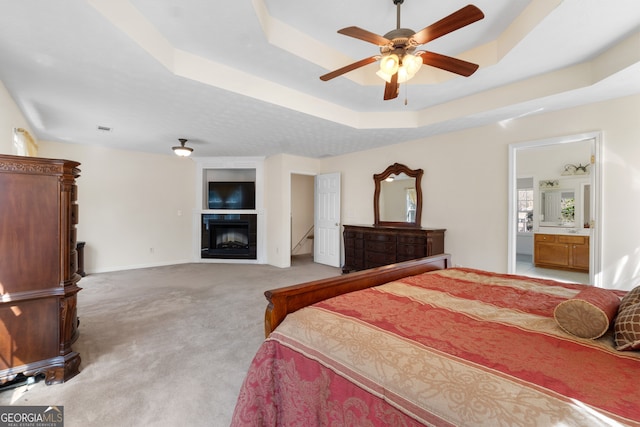 bedroom with light carpet, baseboards, a tile fireplace, ceiling fan, and a tray ceiling