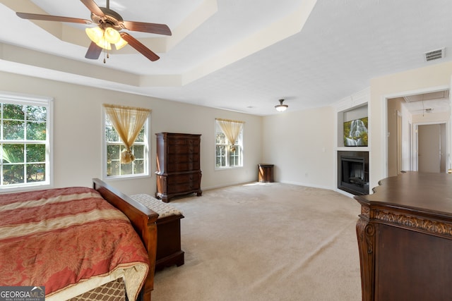 bedroom with attic access, visible vents, a ceiling fan, a tray ceiling, and carpet floors