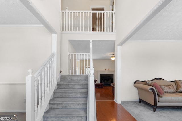 staircase with a fireplace, wood finished floors, a towering ceiling, baseboards, and ornamental molding