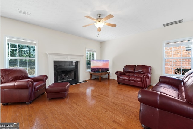 living room featuring a ceiling fan, visible vents, a fireplace, and wood finished floors