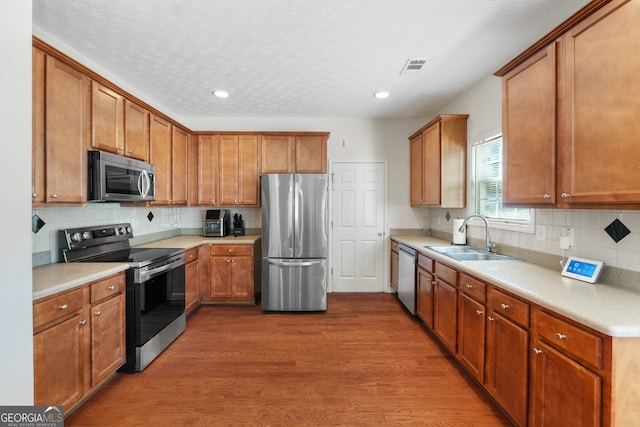 kitchen featuring stainless steel appliances, wood finished floors, a sink, visible vents, and light countertops