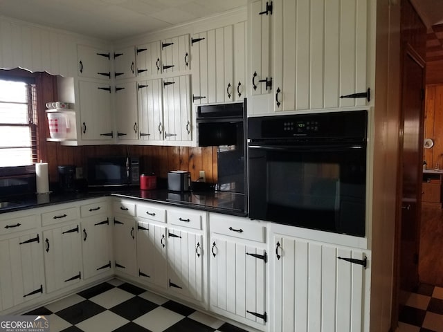 kitchen with white cabinets, dark countertops, light floors, crown molding, and black appliances