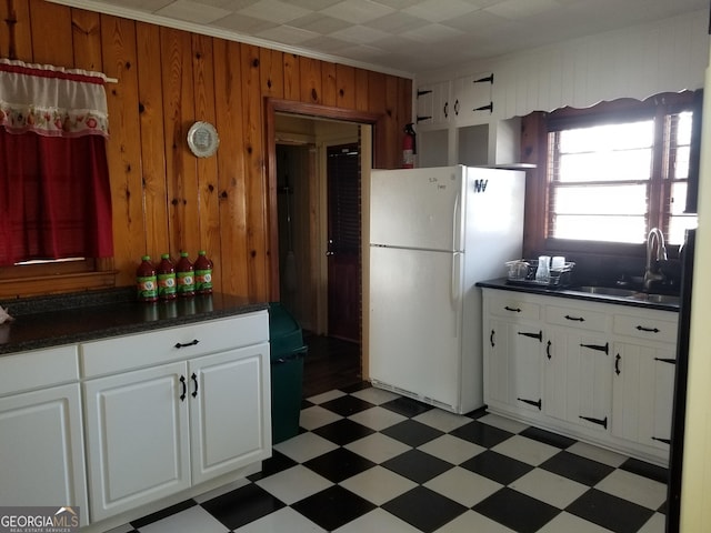 kitchen with wood walls, a sink, freestanding refrigerator, light floors, and dark countertops