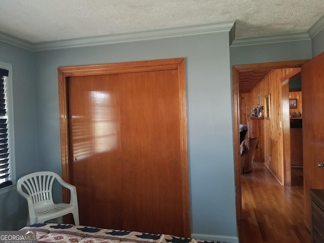 bedroom with wooden walls, crown molding, a textured ceiling, and wood finished floors