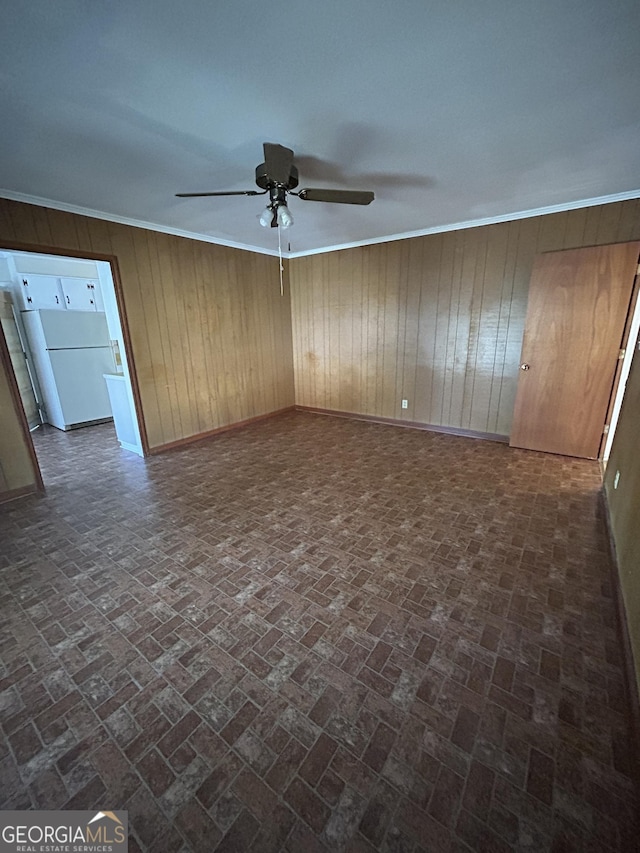 spare room with ornamental molding, brick floor, a ceiling fan, and baseboards