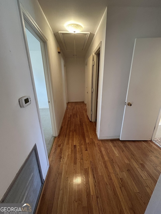 hall with attic access, visible vents, baseboards, and wood finished floors