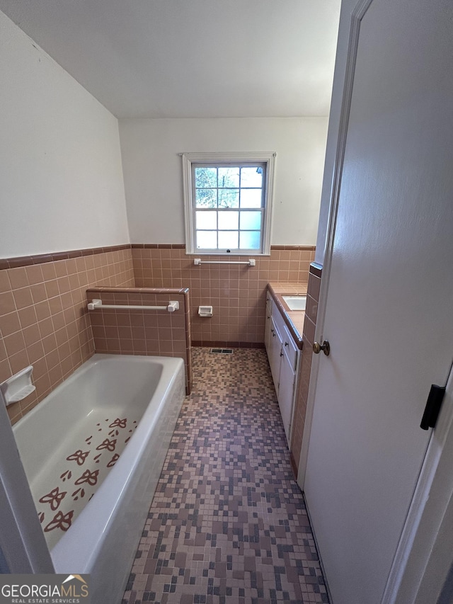 full bath with a bathing tub, vanity, tile walls, and wainscoting