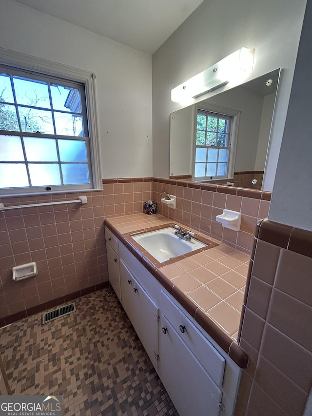 bathroom with a wainscoted wall, tile walls, visible vents, vanity, and tile patterned flooring