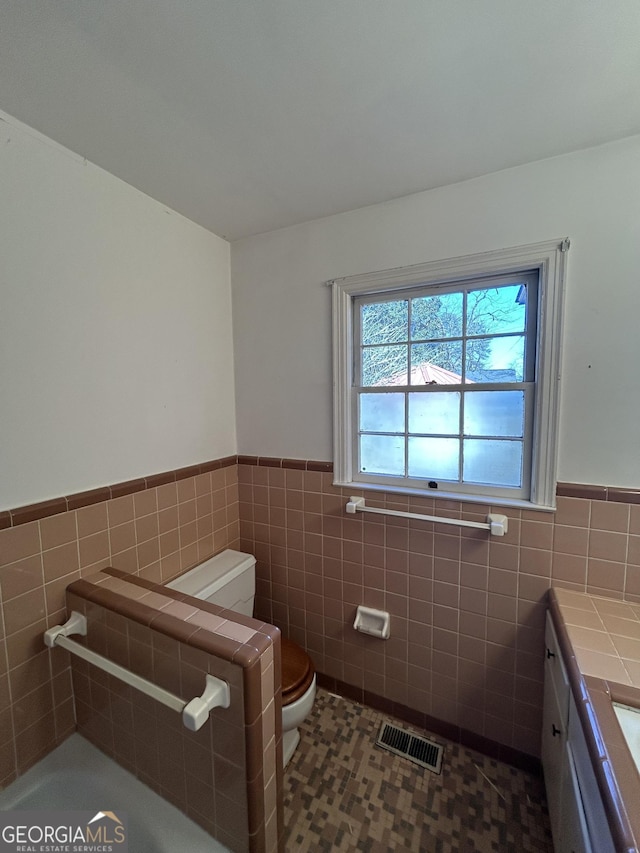 bathroom with toilet, wainscoting, visible vents, and tile walls