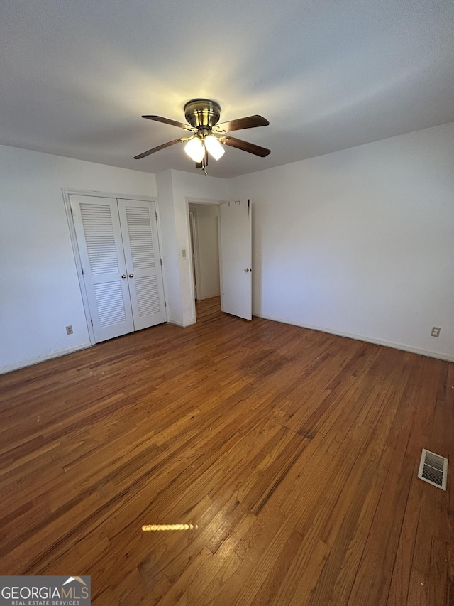unfurnished bedroom featuring ceiling fan, a closet, visible vents, and hardwood / wood-style floors