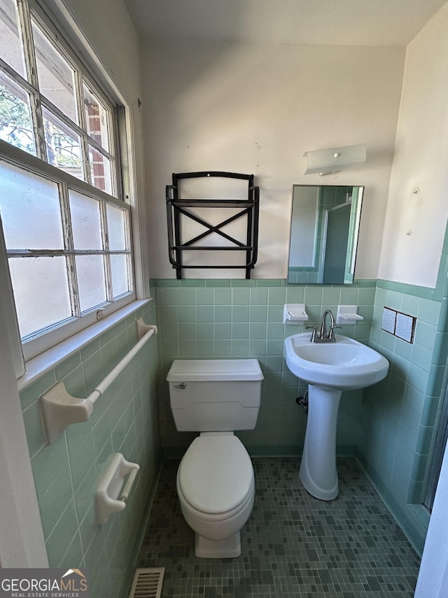 bathroom with tile patterned flooring, toilet, a wainscoted wall, visible vents, and tile walls