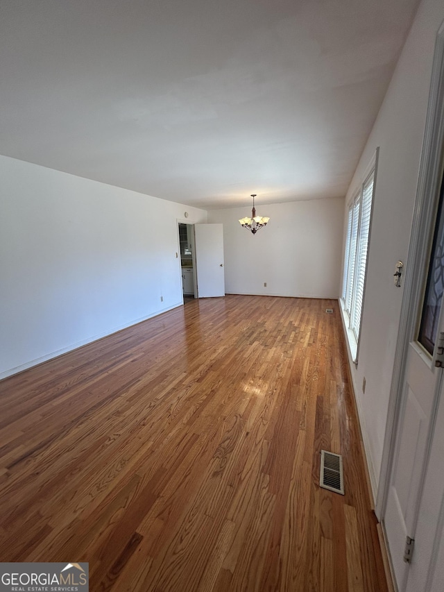 interior space with baseboards, wood finished floors, visible vents, and an inviting chandelier