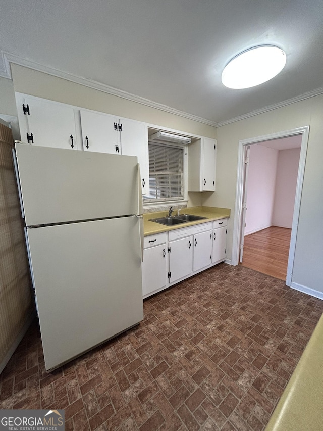 kitchen featuring light countertops, ornamental molding, freestanding refrigerator, white cabinets, and a sink