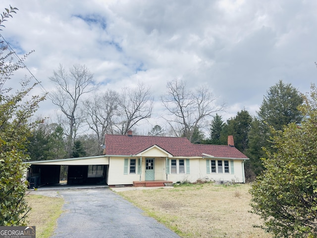 ranch-style house with aphalt driveway, an attached carport, roof with shingles, a chimney, and a front yard