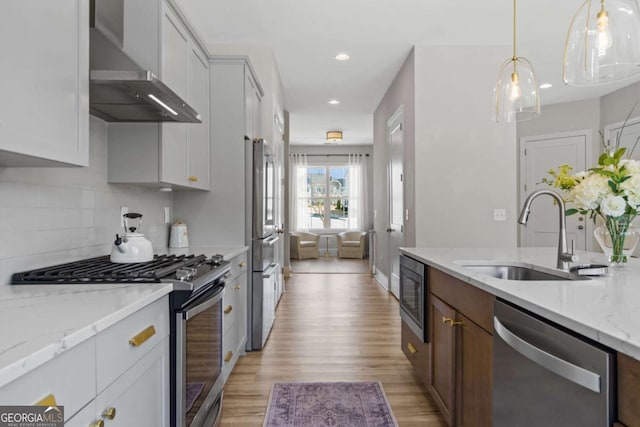 kitchen with decorative backsplash, appliances with stainless steel finishes, light wood-type flooring, wall chimney range hood, and a sink